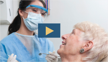 female dental hygenist wearing PPC talking to patient in dental chair