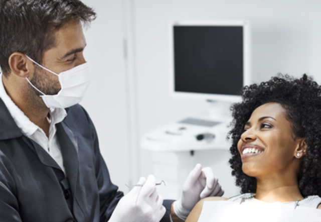male dentist wearing mask talking to patient in dentist chair